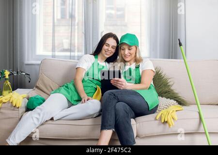 Two female cleaners relaxing on couch and using tablet Stock Photo