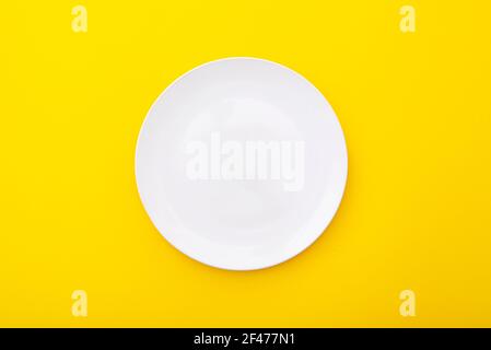 Ceramic white plate on yellow surface, kitchen table, lay out, top view, space for text Stock Photo