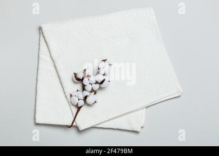 Close-up top view of folded white towel with cotton twig on gray background. Stock Photo
