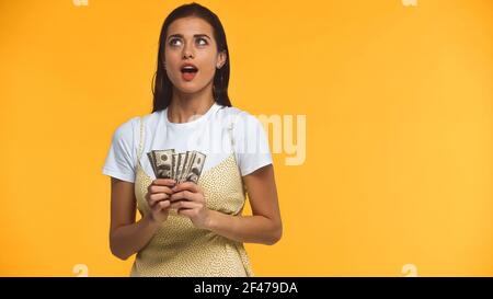 pensive young woman holding dollar banknotes isolated on yellow Stock Photo