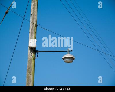 A wooden pylon supporting 230 volt electricity cables, telephone cables and a street lamp in a village in the south west of England. Stock Photo