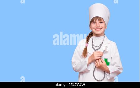 Little, cute girl future doctor dressed white medical apron with stethoscope isolated on blue background, copy space Stock Photo