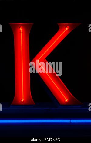 Red glowing neon letter K at night with blue underline Stock Photo