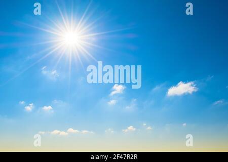 Sun with bright rays in the blue sky with white light clouds, at the horizon a yellowish shade, a gradient Stock Photo