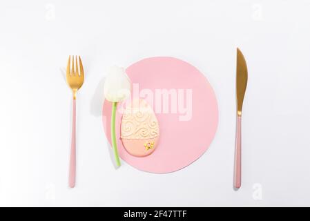 Pastel and colorful easter eggs cookies with tulip and cutlery on pink paper circle, holiday concept Stock Photo
