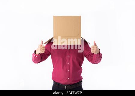 man in a red shirt with a cardboard box on his head makes a gesture with his hands isolated on white background Stock Photo