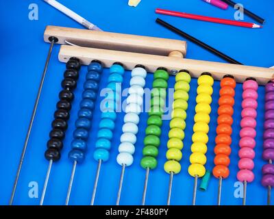 Wooden abacus with multicolored beads on bright blue surface among colored pencils Stock Photo