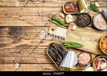 Opened cans conserve with saury, salmon, sprats, sardines, squid and tuna. Wooden background. Top view. Copy space Stock Photo