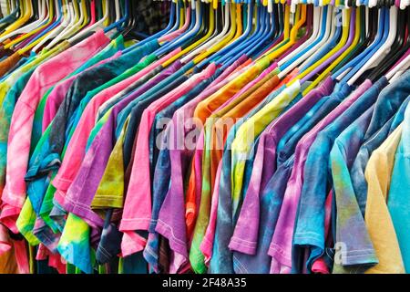 Horizontal sideview of a rack of vibrantly colored tie dyed t-shirts on colored plastic hangers lined up and hanging in a row. Stock Photo