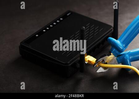 Tearing and cutting with blue wire cutters the network connection of the yellow wire of the Internet connection. Disabling and restricting Internet ac Stock Photo