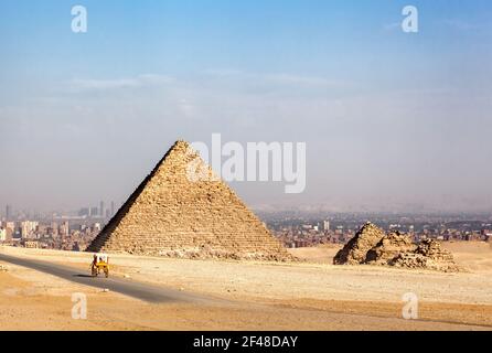 Ancient pyramids of Giza, Cairo. In the foreground, a buggy takes tourists on sightseeing trips around the site, and the smog covered city of Cairo ca Stock Photo