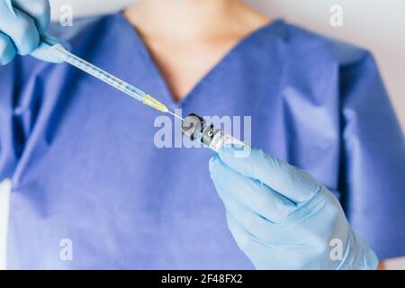 Surgical gloved hands of a nurse withdrawing coronavirus vaccine with a syringe. Stock Photo
