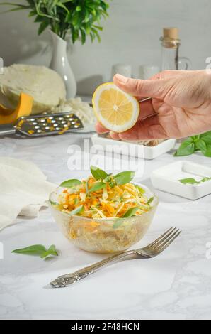 Woman squeezes lemon into a salad of cabbage, grated carrot with basil and rosemary, vertical food photo Stock Photo