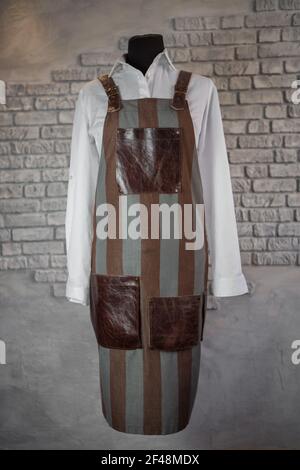 Fabric, striped apron, with leather inserts, for the staff on a mannequin, on a gray background. A uniform. Stock Photo