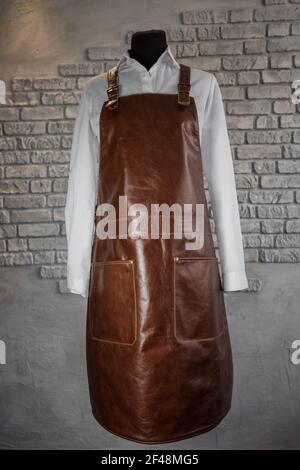 Brown leather apron for staff on a mannequin, on a gray background. Uniform. Stock Photo