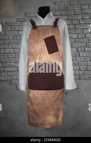Cream apron, with leather inserts, for staff on a mannequin, on a gray background. Uniform. Stock Photo