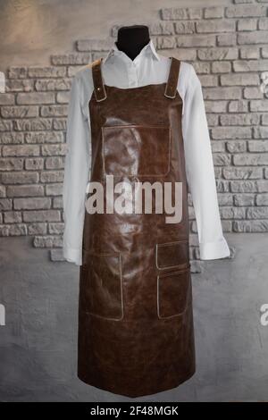 Brown leather apron for staff on a mannequin, on a gray background. Uniform. Stock Photo