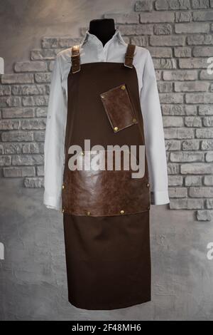Brown apron with leather inserts for staff on a mannequin on a gray background. Uniform. Stock Photo