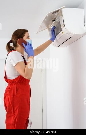Female technician using smartphone and repairing air conditioner Stock Photo