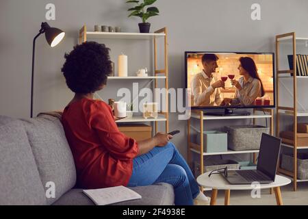 Young woman sitting on couch at home and watching romantic soap opera on television Stock Photo