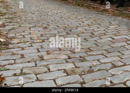 Old street surface paved in heavy stone blocks, grass growing in the cracks, horizontal aspect Stock Photo