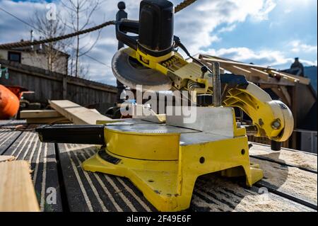 Close up of yellow saw sat on wooden decking being used to construct wooden gazebo roof Stock Photo