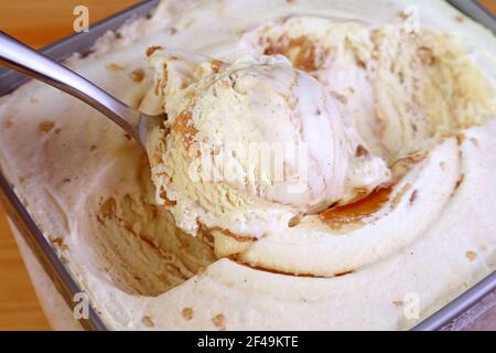 Closeup of a Spoon Scooping Delectable Caramel Macadamia Nut Ice Cream in the Tub Stock Photo