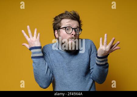 The strange, surprised man shrugs his shoulders and makes a bewildered hand gesture. Yellow background. Stock Photo