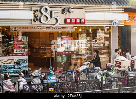 Suzhou, China - May 3, 2010: Closeup of patisserie and coffee shop 85 in street with parked bikes and scooters. People on sidewalk. Stock Photo