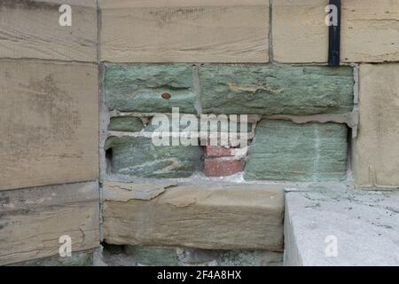 Crumbling and eroded tan and green limestone wall revealing brick behind and sturdier mortar, effects of acid rain, horizontal aspect Stock Photo