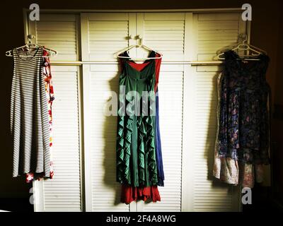 Ironed colorful women's dresses hanging from an old vintage wardrobe wooden knob Stock Photo