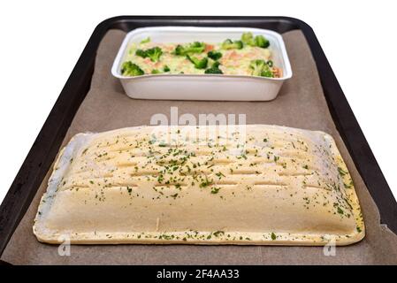 Frozen puff pastry with salmon and pollock fillet with broccoli and roasted almonds in a cream sauce lying on baking paper, isolated on a white backgr Stock Photo