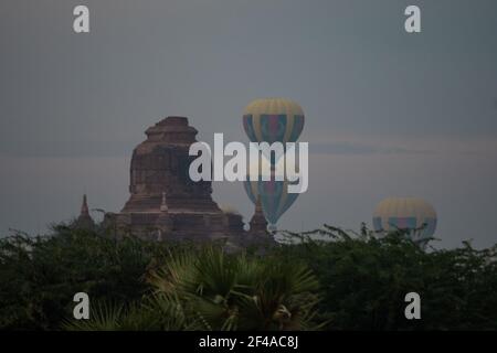 BAGAN, NYAUNG-U, MYANMAR - 2 JANUARY 2020: A few hot air balloons rises behind a historic pagoda temple Stock Photo