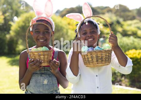 Happy african american brother and sister in bunny ears holding baskets of easter eggs Stock Photo