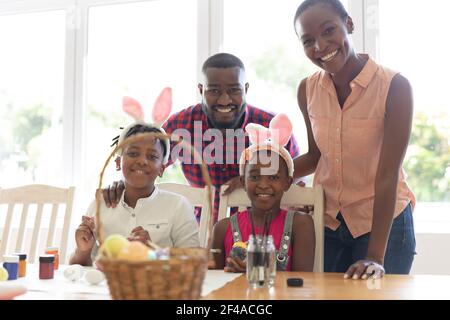 Portrait of happy african american parents with son and daughter in bunny ears painting easter eggs Stock Photo