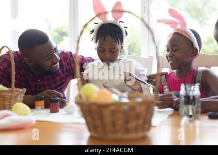 African american father with son and daughter wearing bunny ears painting easter eggs Stock Photo