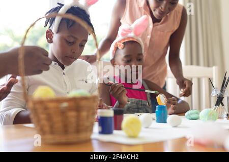 African american mother with son and daughter wearing bunny ears painting easter eggs Stock Photo