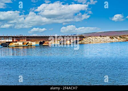 Lake with steel and concrete bridge crossing over the inlet under bright blue skies with white fluffy clouds. Stock Photo