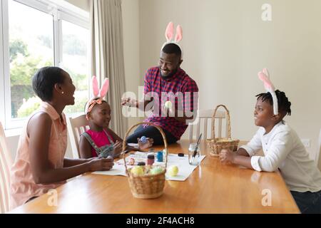 Happy african american parents with son and daughter wearing bunny ears painting easter eggs Stock Photo