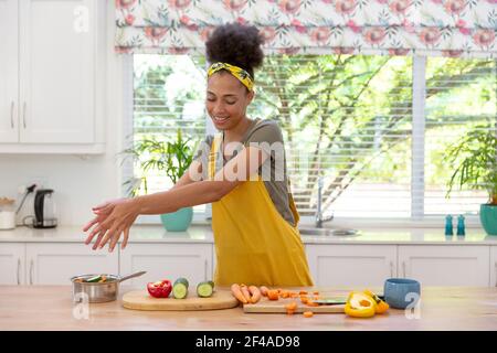 Mixed race woman cutting vegetables and smiling in a kitchen Stock Photo