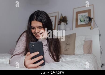 A beautiful Caucasian female using her smartphone while lying on the bed Stock Photo