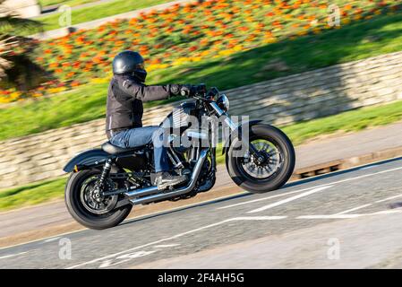 Harley Davidson Forty Eight motorcycle being ridden in Southend on Sea, Essex, UK on a bright sunny day, passing the Cliff Gardens Stock Photo