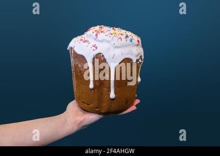 Hand holding easter traditional sweet bread, paska decorated with sugar icing isolated on blue background. Orthodox handmade kulich with topping. Spri Stock Photo