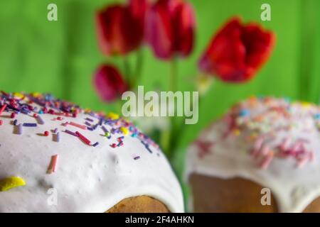 Easter holidays sweet bread close-up, paska decorated with sugar icing with red tulip flowers on green background. Orthodox traditional handmade kulic Stock Photo