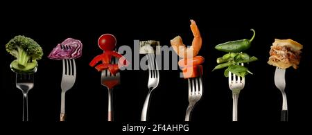 Different food impaled on forks against dark background Stock Photo
