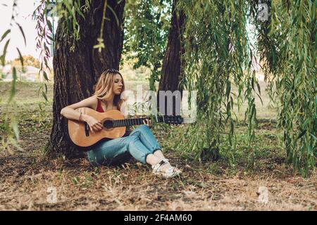 Creative hobbies, guitar lessons, playing musical instruments. Acoustic guitars for beginners. Young blonde woman with Acoustic guitar outdoor Stock Photo
