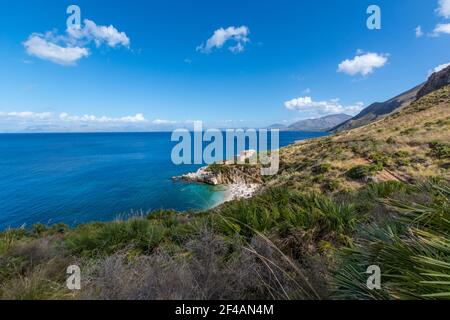 A landscape of rocks and hills surrounded by the sea under a blue sky ...