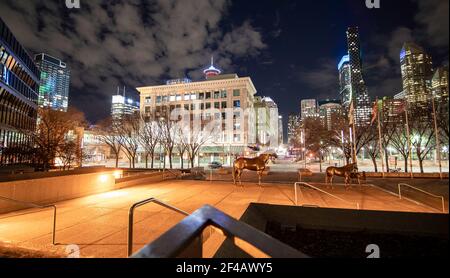 Calgary Alberta Canada, March 15 2021: A quiet downtown plaza at night with horse sculptures and downtown office buildings and landmarks at night in a