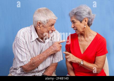 An old grey haired couple, a man and a woman in red having an active conversation isolated against a blue background. Stock Photo