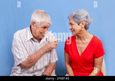 An old grey haired couple, a man and a woman having an active conversation isolated against a blue background. Stock Photo
